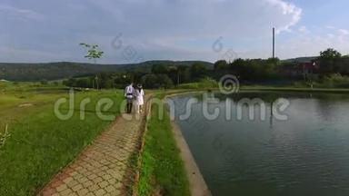 婚礼当天，新娘和新郎沿着湖边散步的空中景色。 新婚夫妇穿着传统西装
